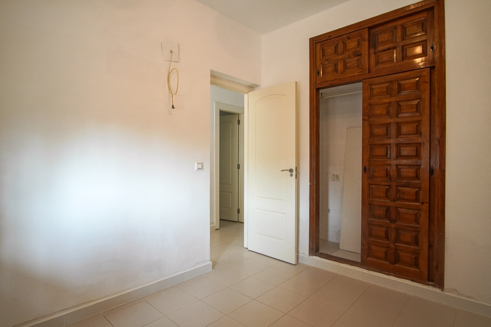 Chambre avec placard intégré en bois sculpté et sol en grès. La pièce communique avec le couloir et offre un potentiel de rénovation personnalisée.