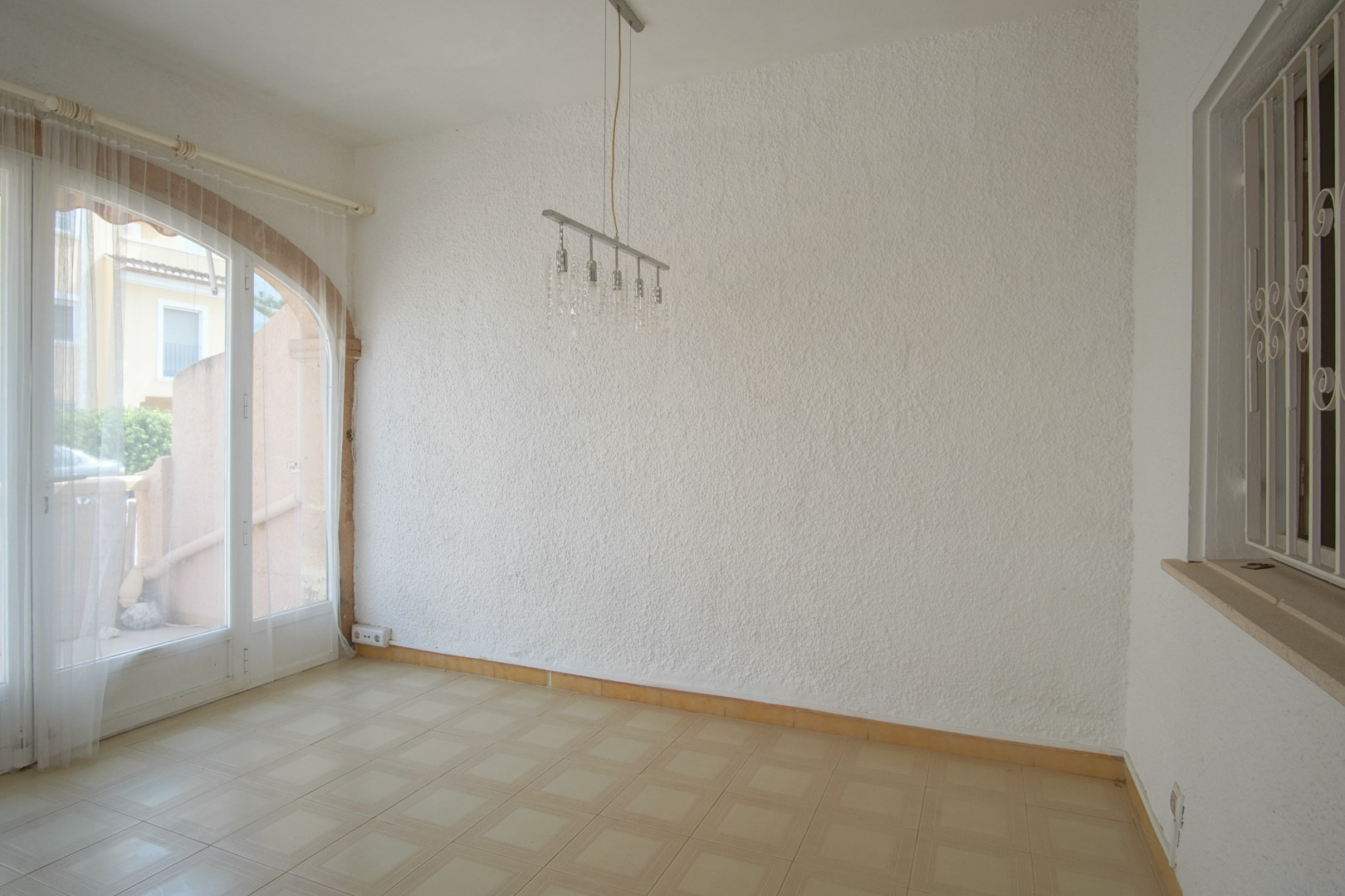 Espace de vie avec murs à crépi, sol carrelé et une porte-fenêtre voûtée offrant une luminosité naturelle et un accès extérieur.