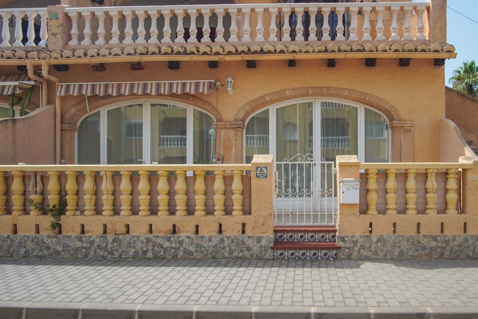 Façade extérieure au rez-de-chaussée avec balustrade classique, portillon en métal blanc et grandes baies vitrées cintrées ouvrant sur la terrasse.
