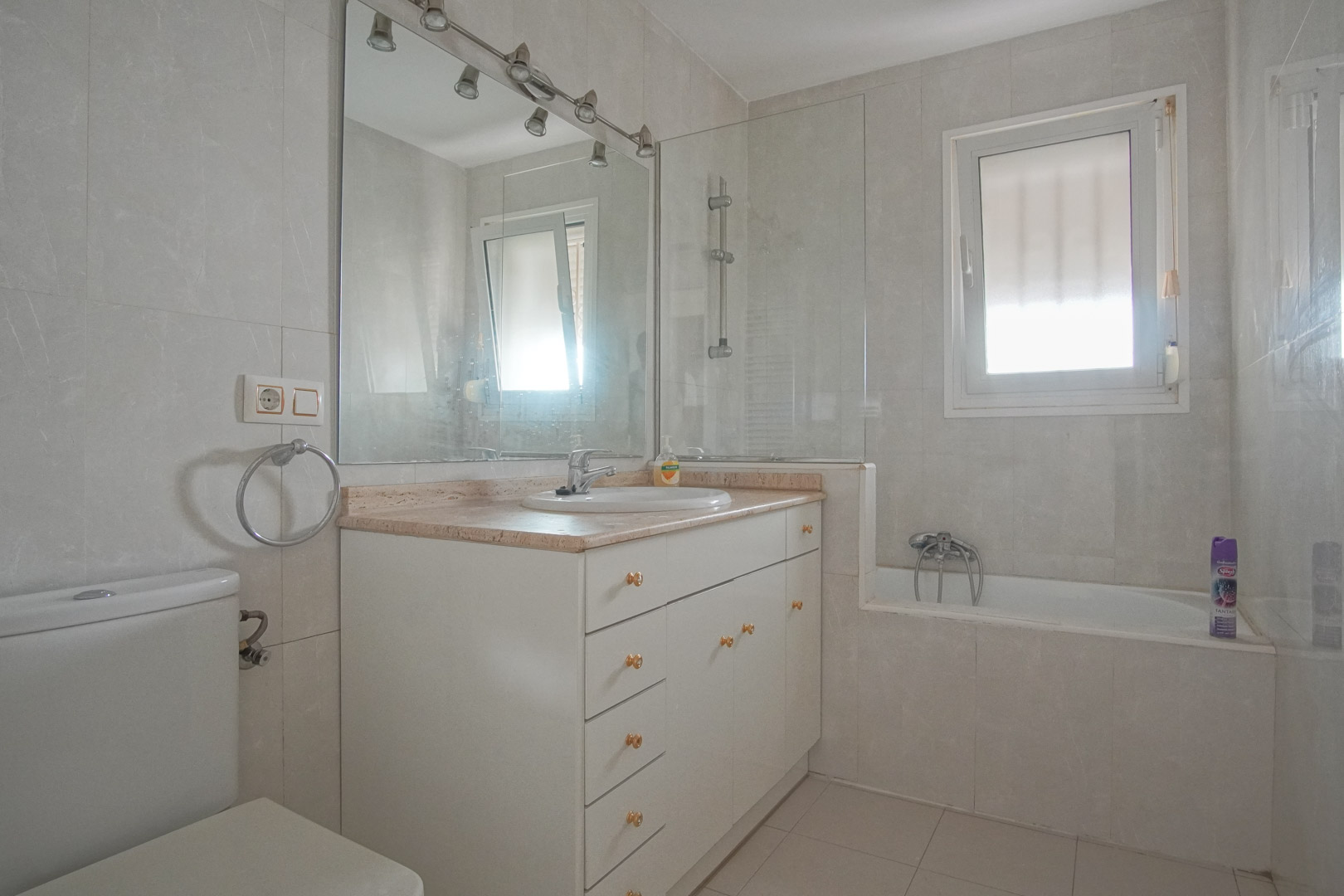 Salle de bain avec meuble vasque blanc, plan de travail en marbre et baignoire avec paroi en verre. La pièce bénéficie d'une fenêtre pour la lumière naturelle.