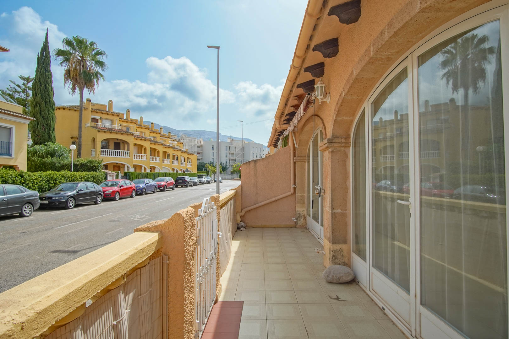 Terrasse extérieure avec sol en céramique et grandes baies vitrées cintrées, offrant une vue sur la rue résidentielle et l'architecture locale de Dénia.