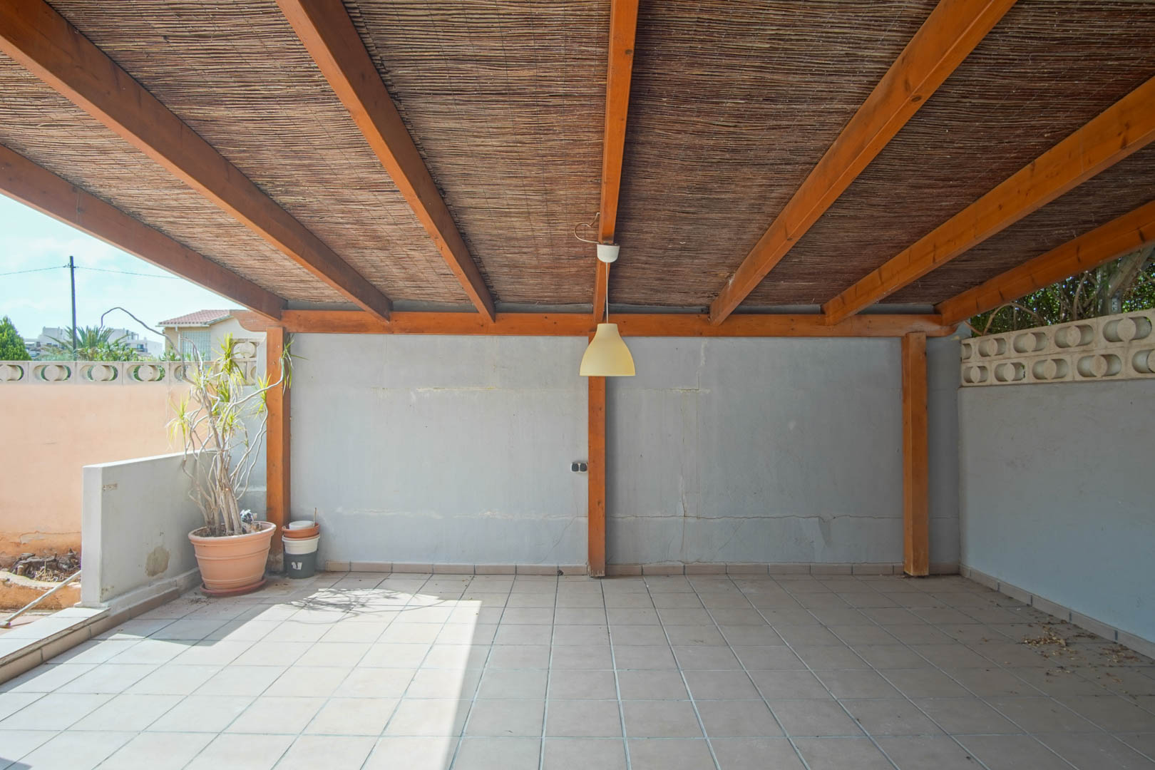 Terrasse extérieure couverte avec structure en poutres de bois, toiture en canisse, sol carrelé et murs avec claustras décoratifs.
