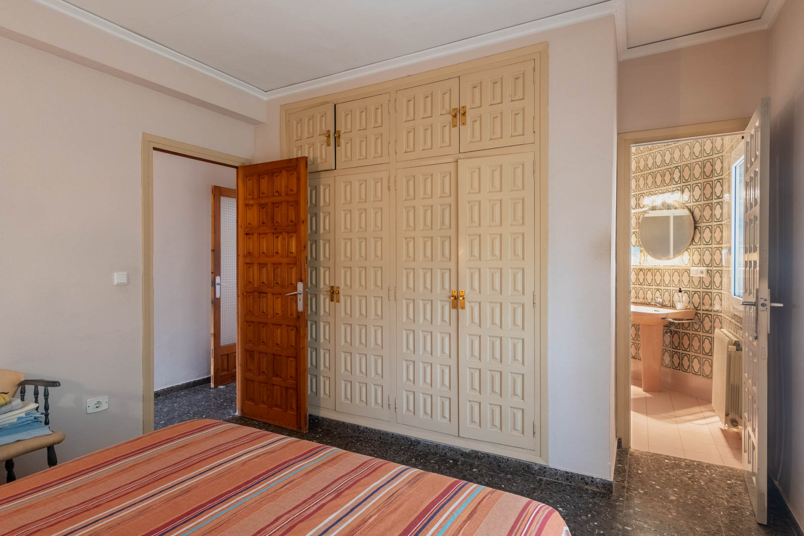 Chambre avec grand placard encastré aux portes travaillées et salle de bain attenante décorée de carreaux géométriques et baignée de lumière naturelle.
