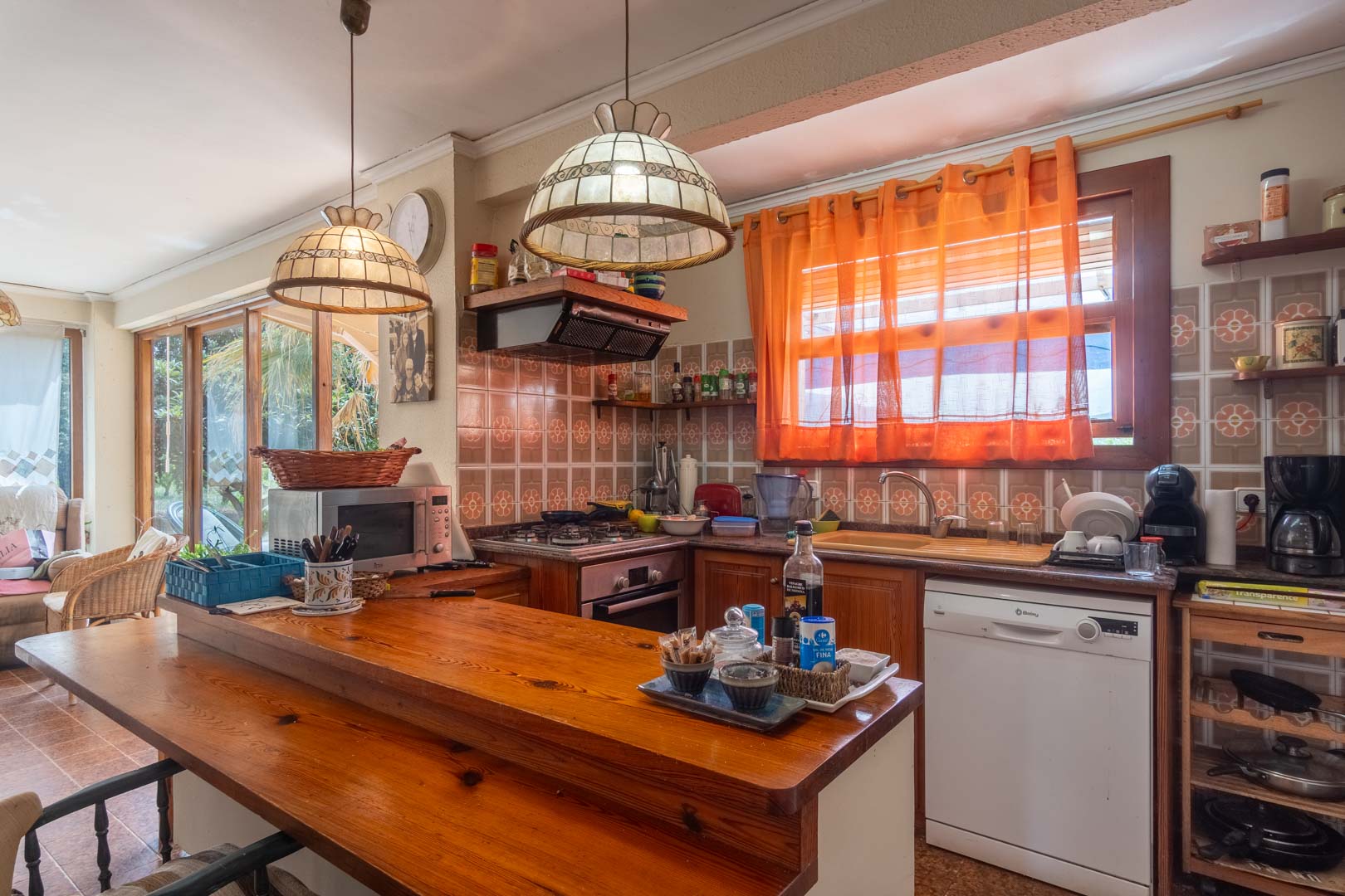 Cuisine rustique avec bar en bois massif, crédence en carrelage traditionnel et suspensions décoratives. L'espace est ouvert et fonctionnel.