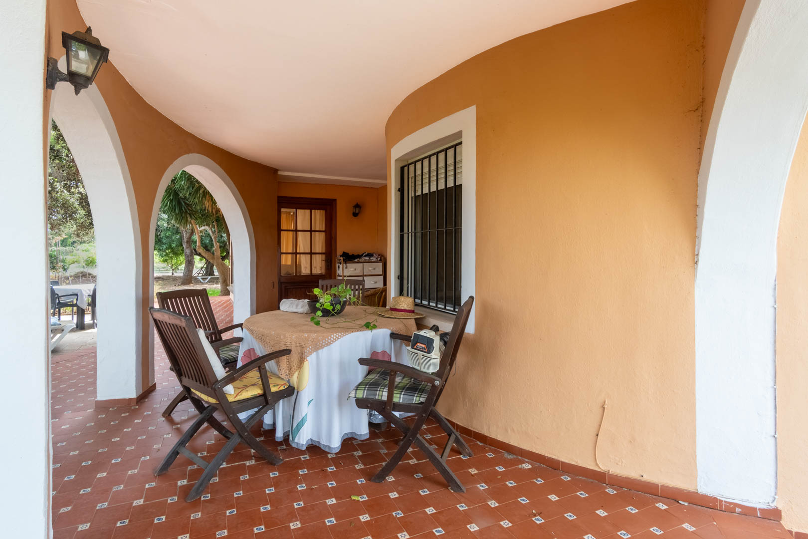 Porche couvert avec des arches blanches et un sol en terre cuite. Cet espace de repas extérieur ombragé donne sur le jardin méditerranéen de la propriété.