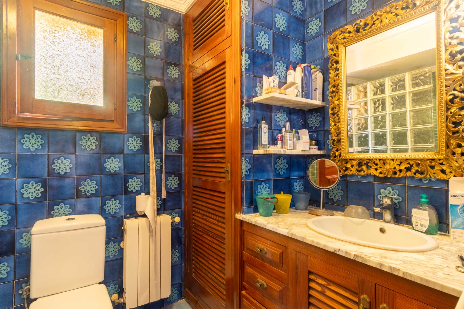 Salle de bain avec carrelage bleu à motifs, meuble sous vasque en bois avec plan en marbre et miroir doré sculpté de style traditionnel.