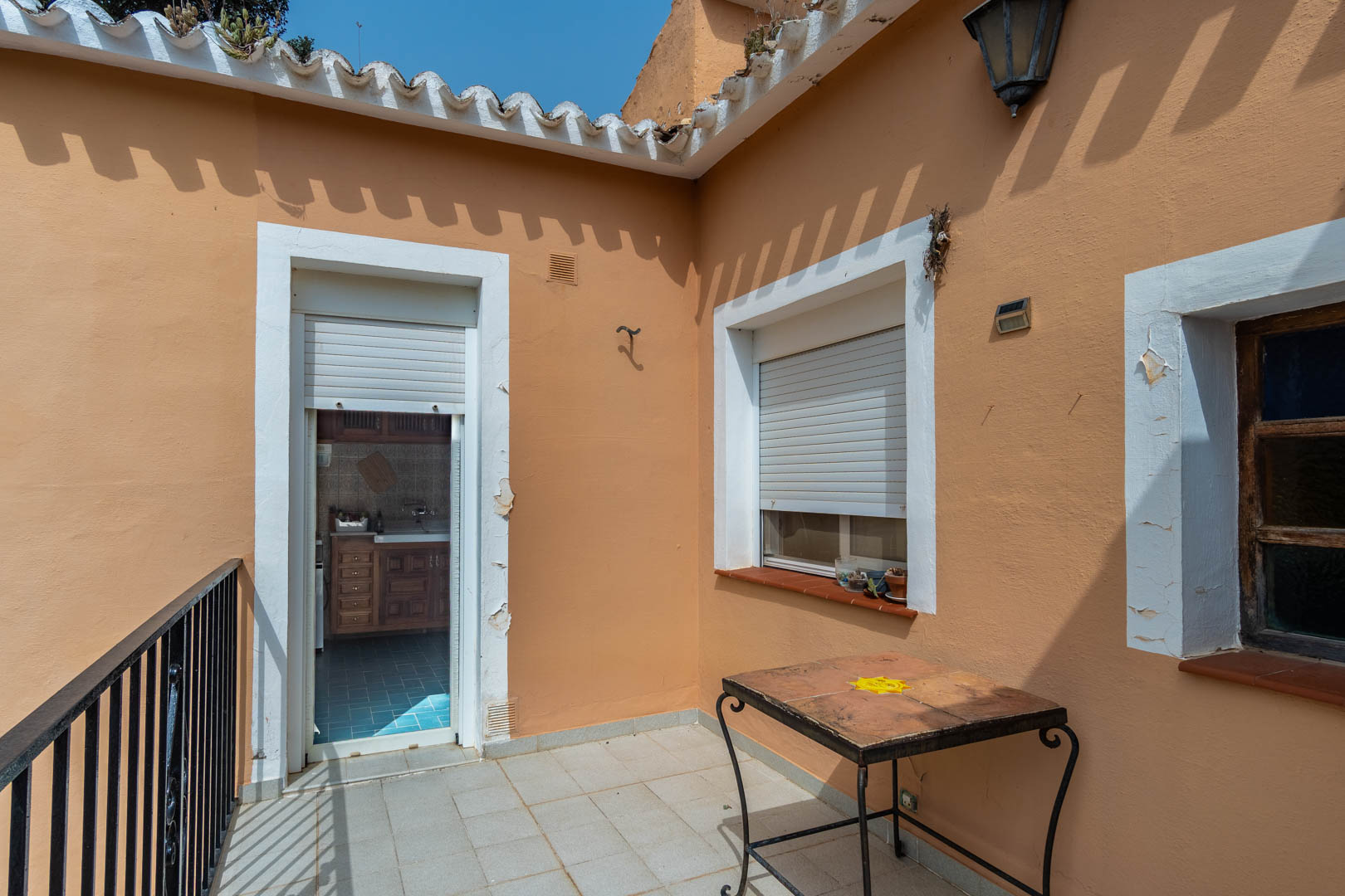Terrasse supérieure avec sol carrelé et garde-corps en fer forgé, communiquant directement avec la cuisine indépendante par une porte à volet.