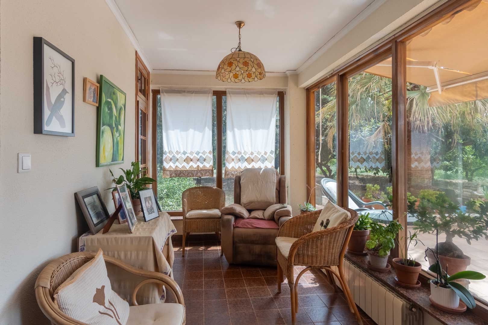 Terrasse vitrée dotée de menuiseries en bois et d'un sol en carrelage. Un espace lumineux avec vue sur le jardin et mobilier en osier pour la détente.