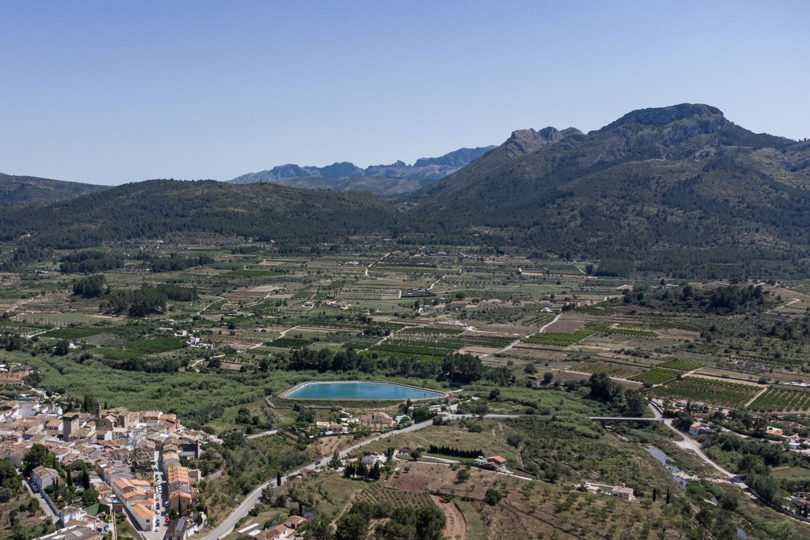 Vue aérienne panoramique de la vallée de Jalón depuis Alcalalí, illustrant les paysages ruraux, un réservoir turquoise et les massifs montagneux environnants.