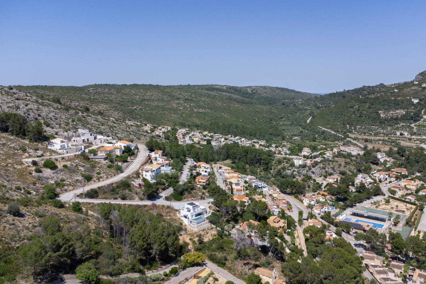 Vue aérienne panoramique du Residencial Vall de Pop à Alcalalí, illustrant l'intégration des villas blanches sur les versants verdoyants de la vallée de Jalón.