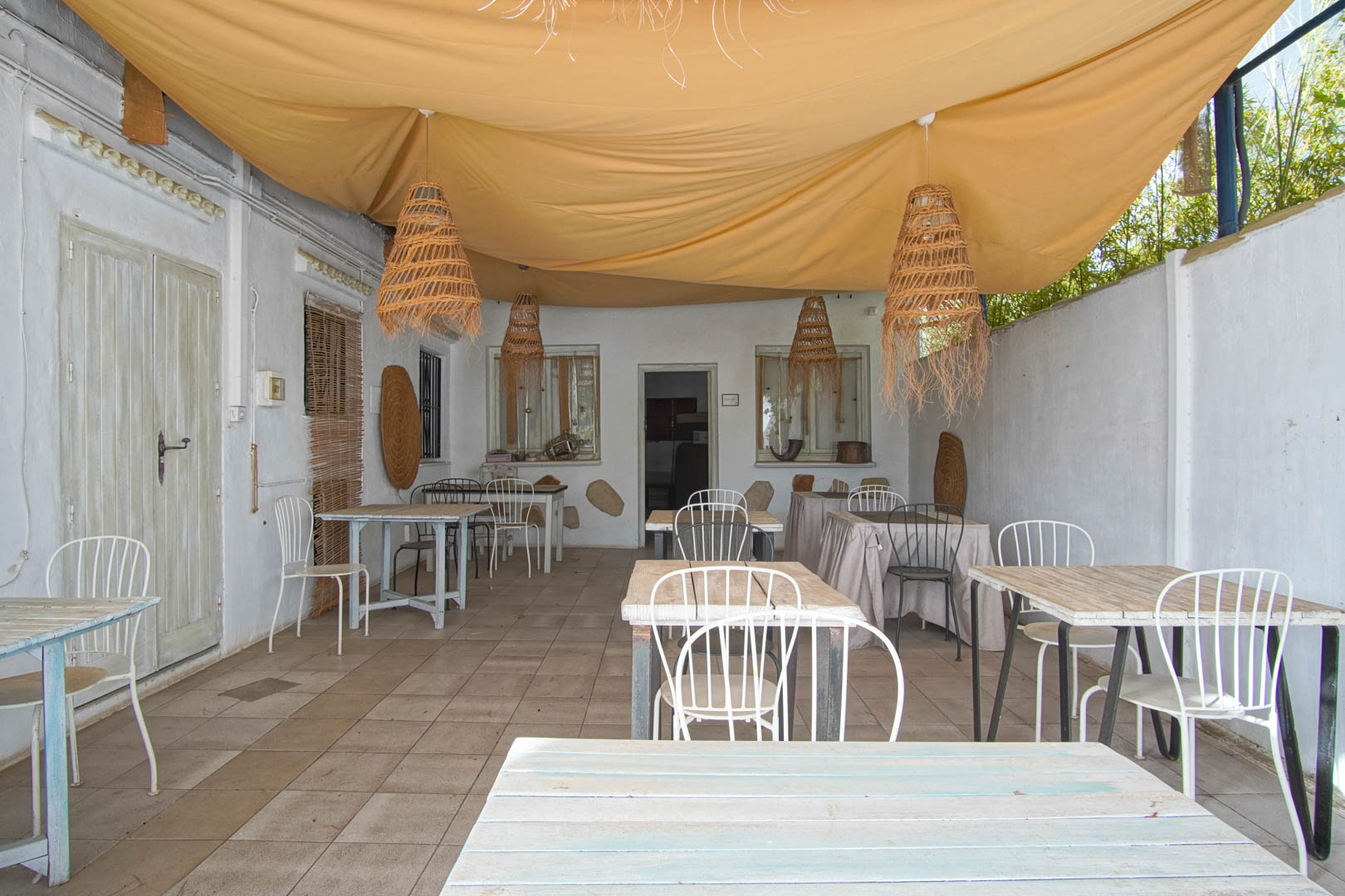 Porche de restaurant avec tables en bois et suspensions en osier sous un auvent.