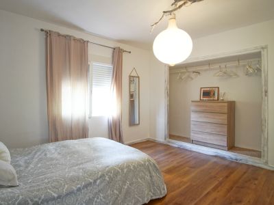 Chambre lumineuse avec lit double, rideaux roses et dressing ouvert avec commode en bois clair.