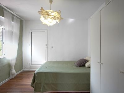 Chambre lumineuse avec lit recouvert de lin vert, lampe design et armoire intégrée blanche.