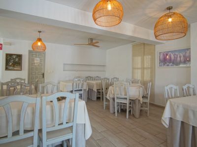 Salle de restaurant avec tables dressées, chaises en bois clair et suspensions en osier.