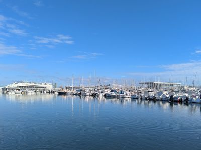Vue du port de plaisance de Denia, présentant plusieurs bateaux et des reflets sur l'eau sous un ciel bleu.