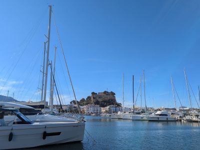 Vue sur le port de plaisance de Denia avec le château historique au loin sous un ciel bleu clair.