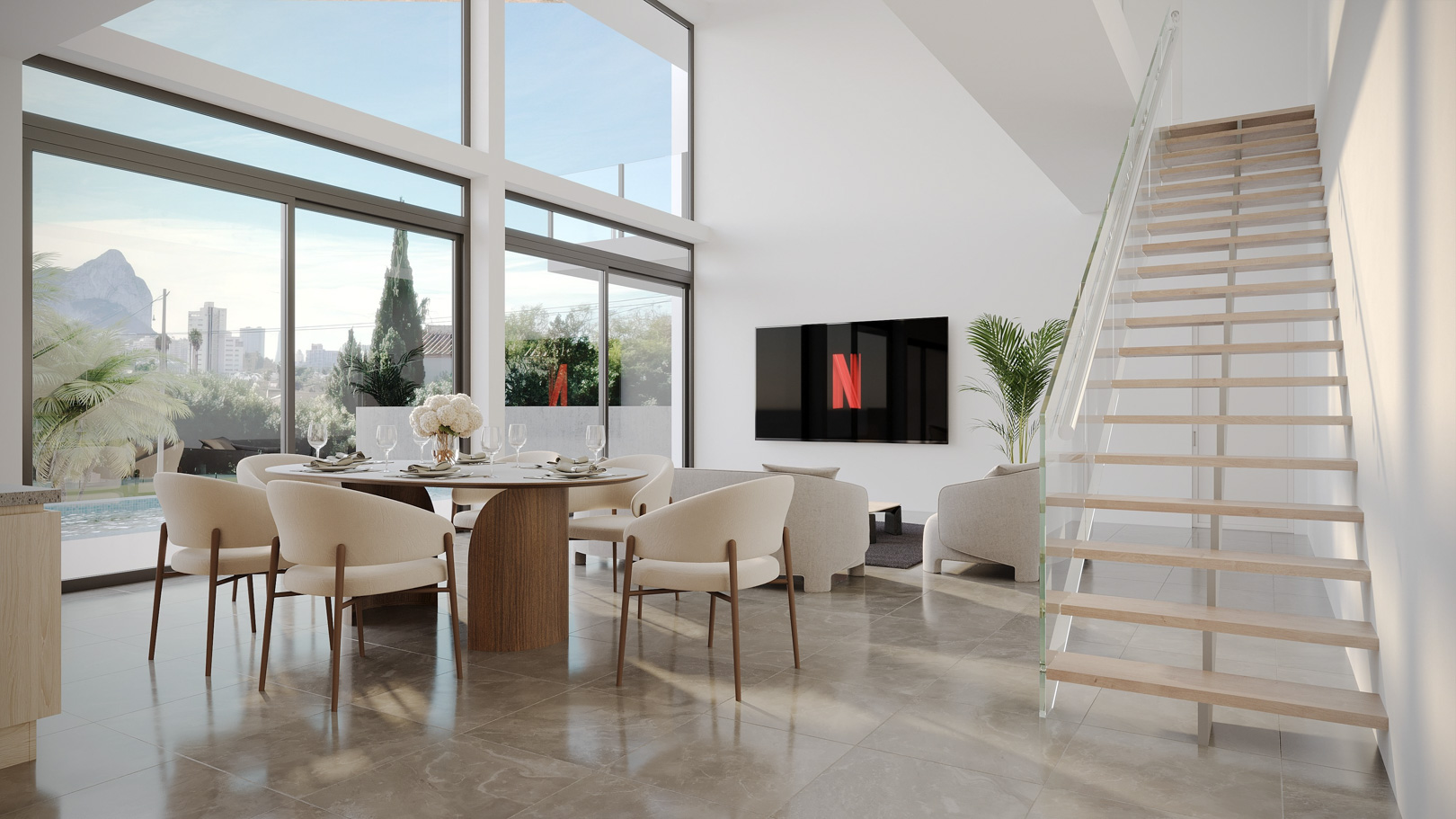 Salon-salle à manger à double hauteur avec de grandes baies vitrées offrant une vue sur le Peñón de Ifach et un escalier suspendu en bois et verre.
