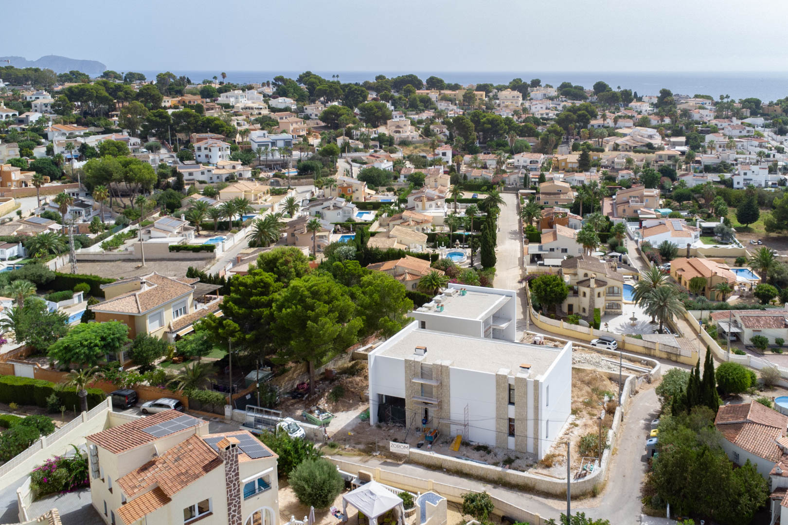 Vue aérienne de la villa en cours de construction, présentant une façade blanche avec des détails en pierre dans un quartier résidentiel avec vue sur mer.