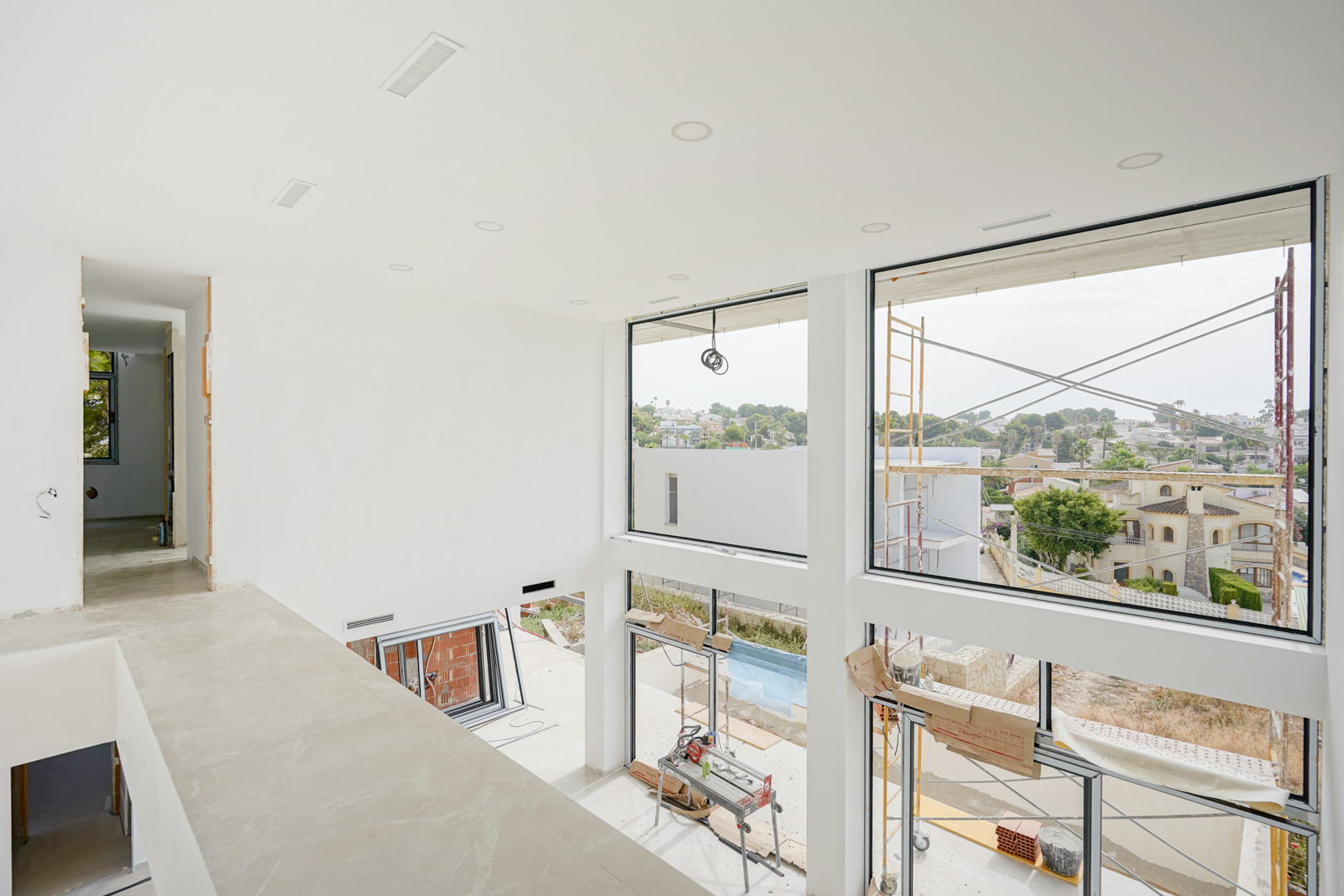 Vue de l'étage sur le salon à double hauteur avec de grandes baies vitrées, des spots encastrés et des bouches de climatisation intégrées.