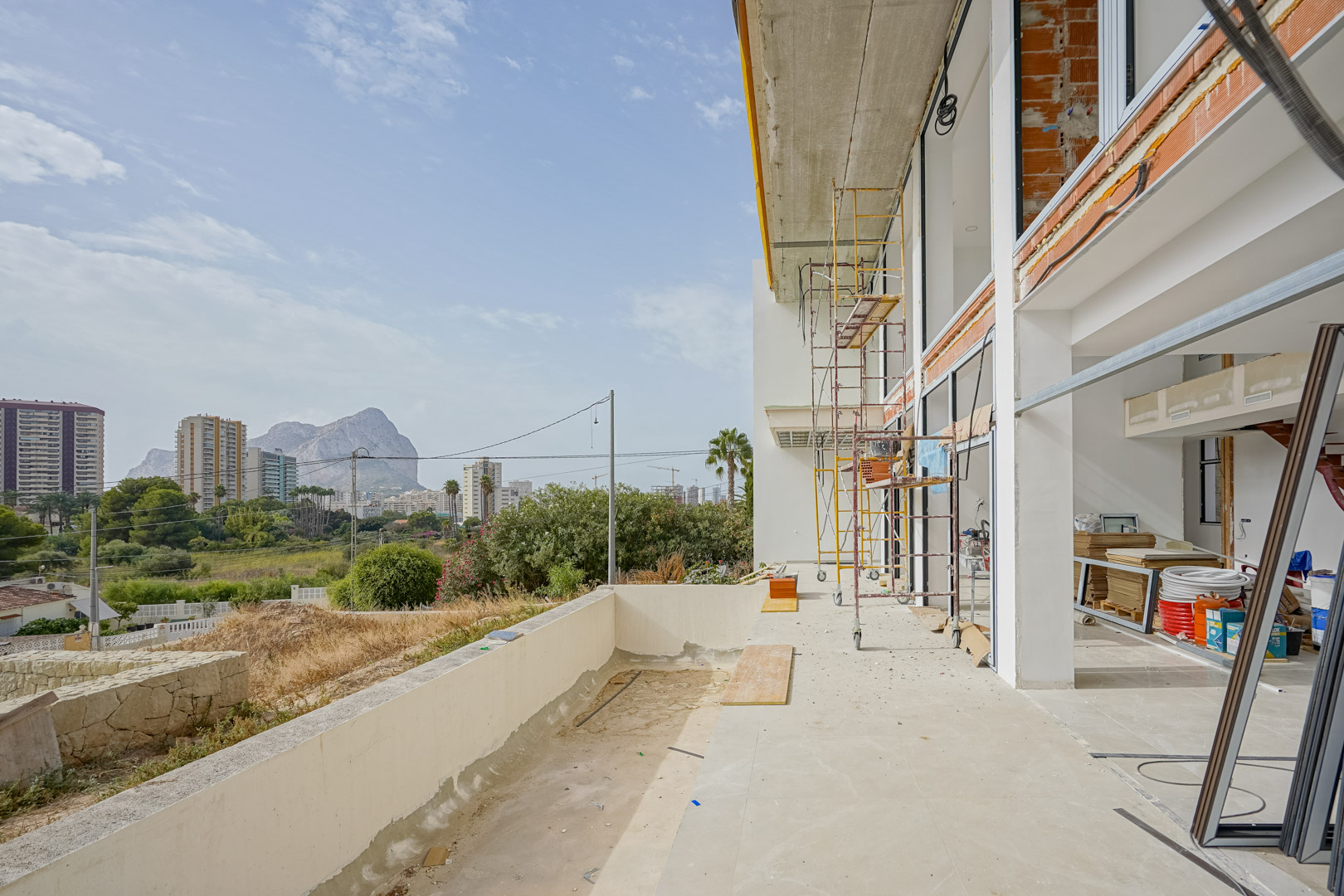 Vue extérieure de la villa en construction avec échafaudages, montrant les grandes baies vitrées et la terrasse offrant une vue sur le Peñón de Ifach.