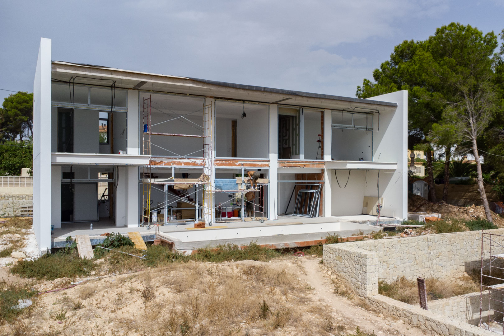 Vue extérieure de la villa en construction illustrant la structure blanche à deux étages, les larges ouvertures et la zone de la piscine.