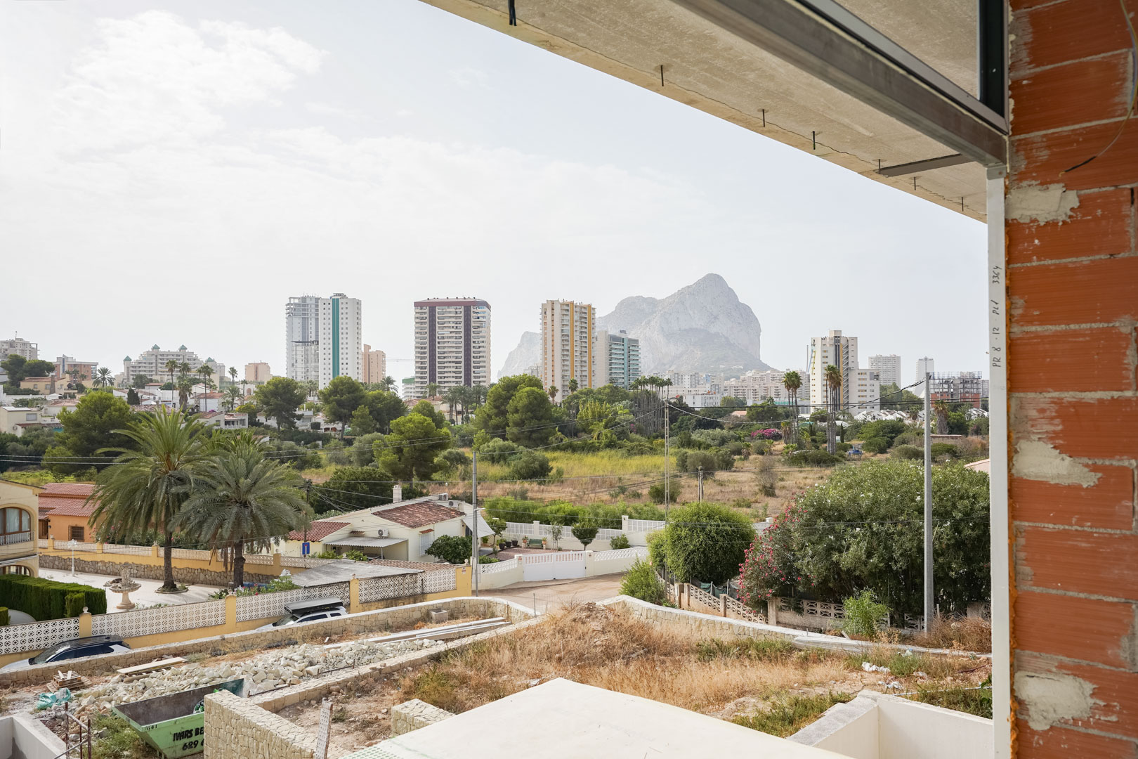 Vue panoramique depuis l'étage en construction, surplombant le Peñón de Ifach et la silhouette de Calpe, encadrée par des murs en briques et des dalles en béton.