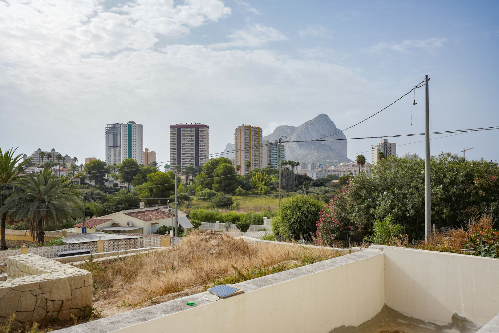 Vues dégagées sur le Peñón de Ifach et les gratte-ciels de Calpe depuis le terrain surélevé de la future villa, entouré de verdure.