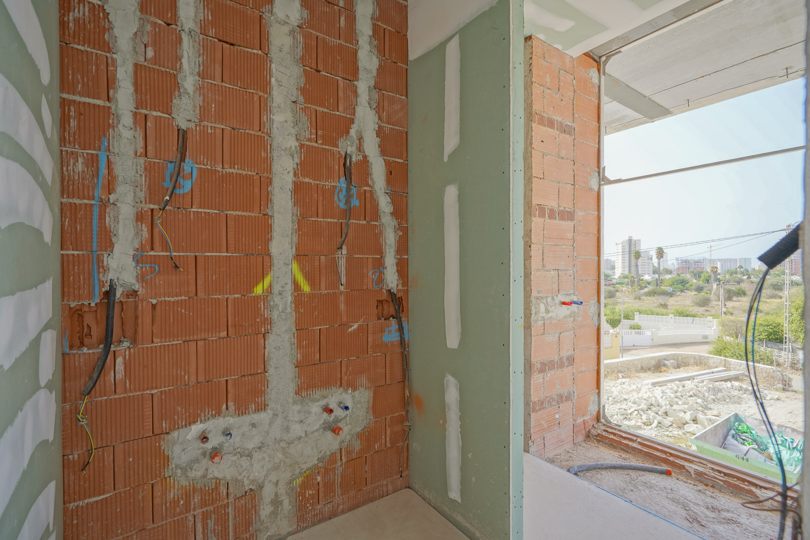 Aperçu de l'avancement des travaux avec murs en briques, installations électriques et plomberie apparente à côté d'une grande ouverture vitrée.