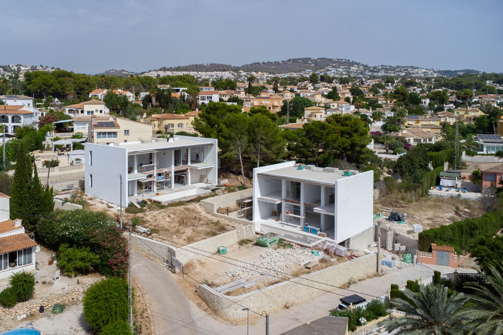 Vue aérienne de deux villas modernes en construction à Calpe, illustrant l'architecture cubique blanche et les murs de soutènement en pierre sèche.