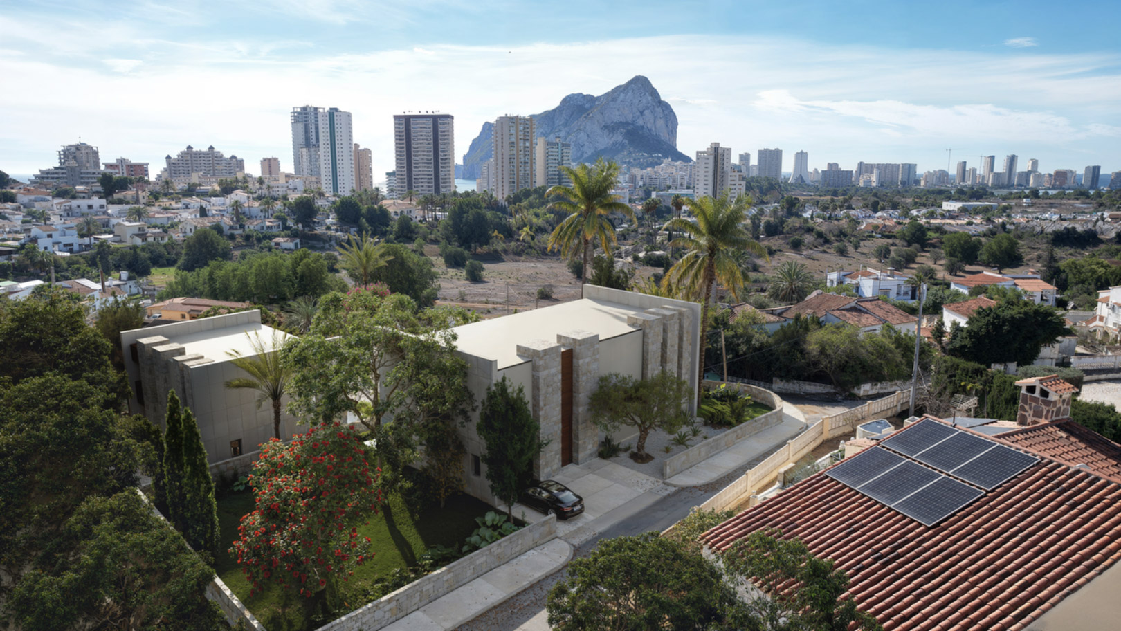 Vue aérienne de la villa moderne aux façades en pierre naturelle, entourée de jardins paysagers avec le Peñón d'Ifach en arrière-plan à Calpe.
