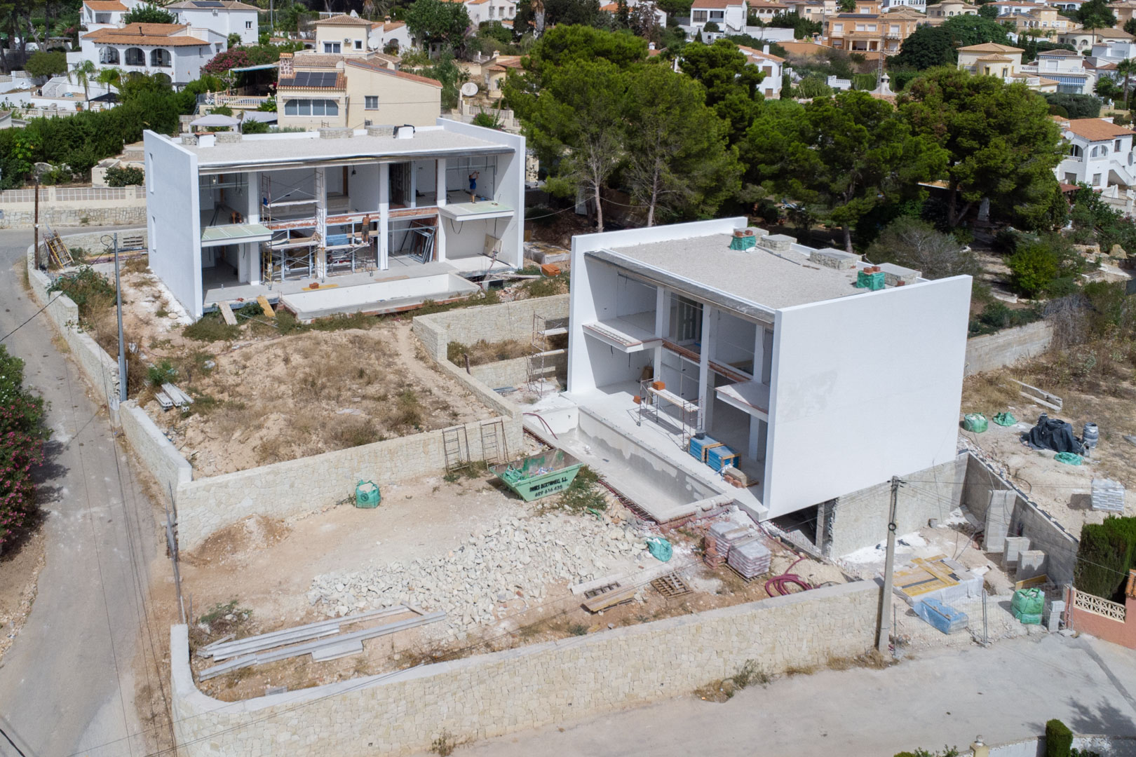 Vue aérienne de l'état d'avancement des travaux, illustrant la structure des deux villas modernes avec leurs murs d'enceinte en pierre naturelle et l'aménagement des parcelles.