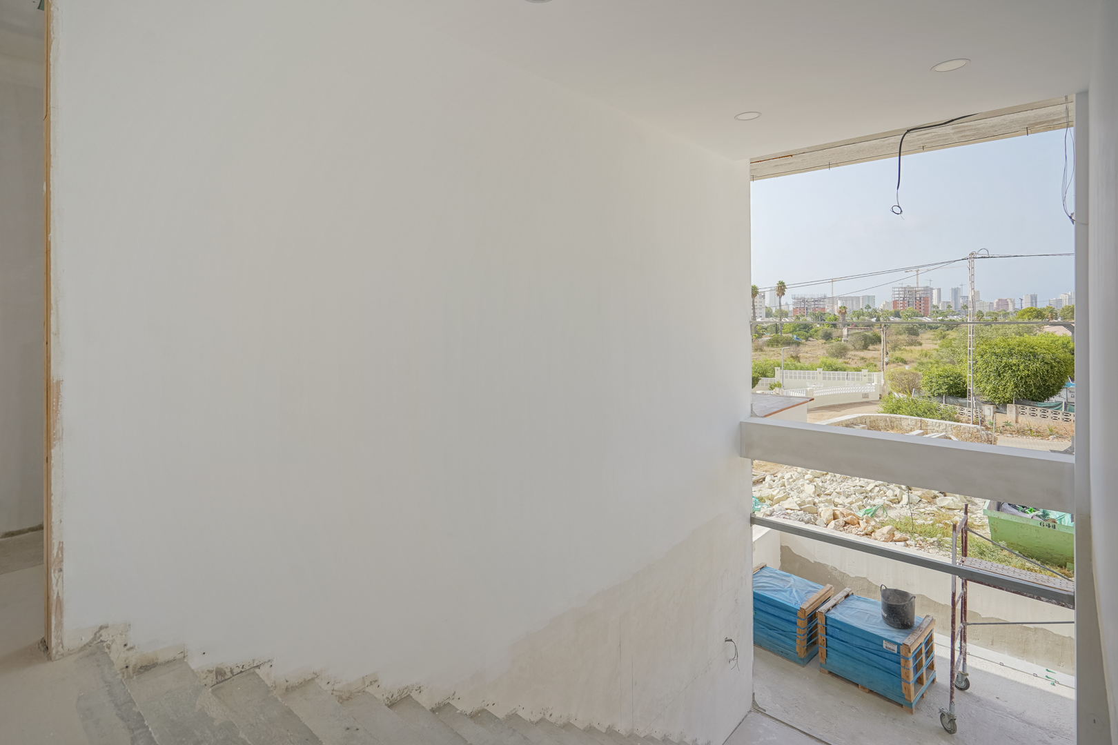 Vue depuis l'escalier en chantier révélant une large ouverture vitrée et le panorama urbain de Calpe en cours de développement.