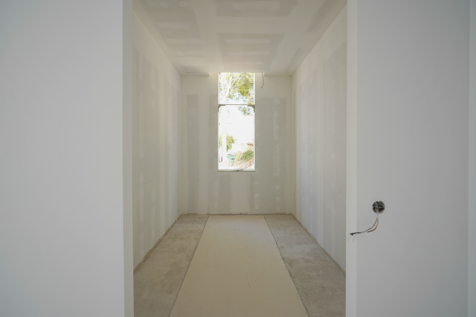 Vue intérieure du dressing en cours de construction, avec une fenêtre verticale apportant de la lumière naturelle et des cloisons en plaques de plâtre.