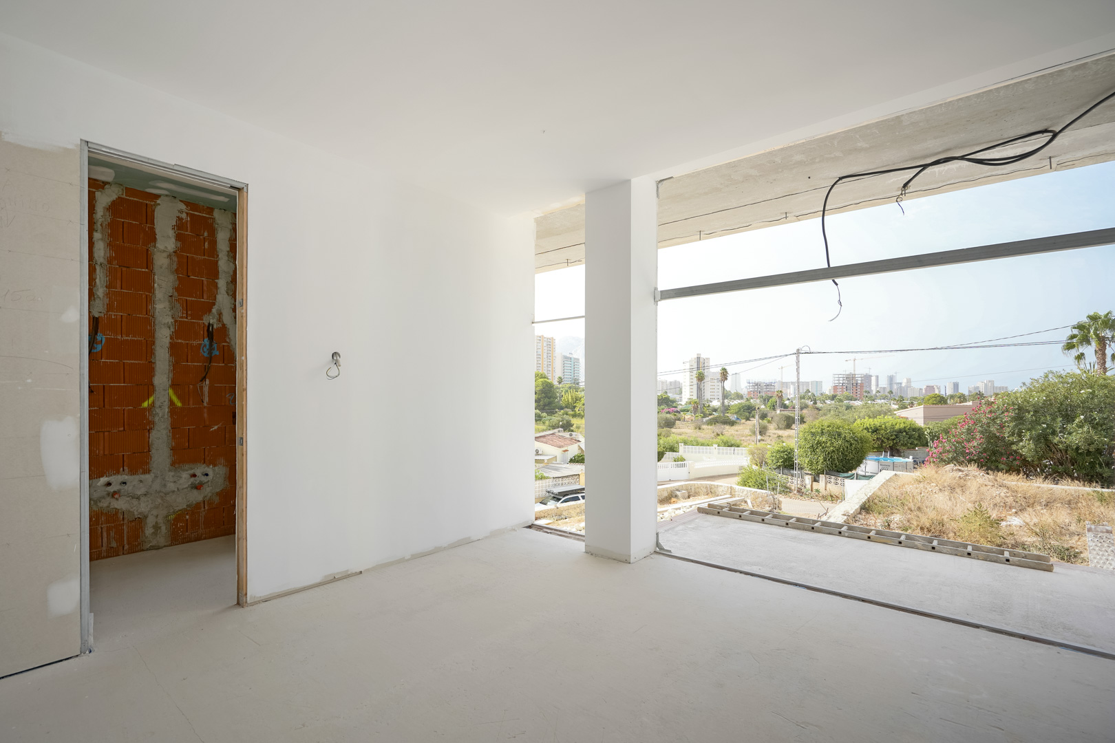 Vue intérieure d'une pièce en cours de construction avec de larges ouvertures offrant un panorama sur Calpe et le rocher d'Ifach.