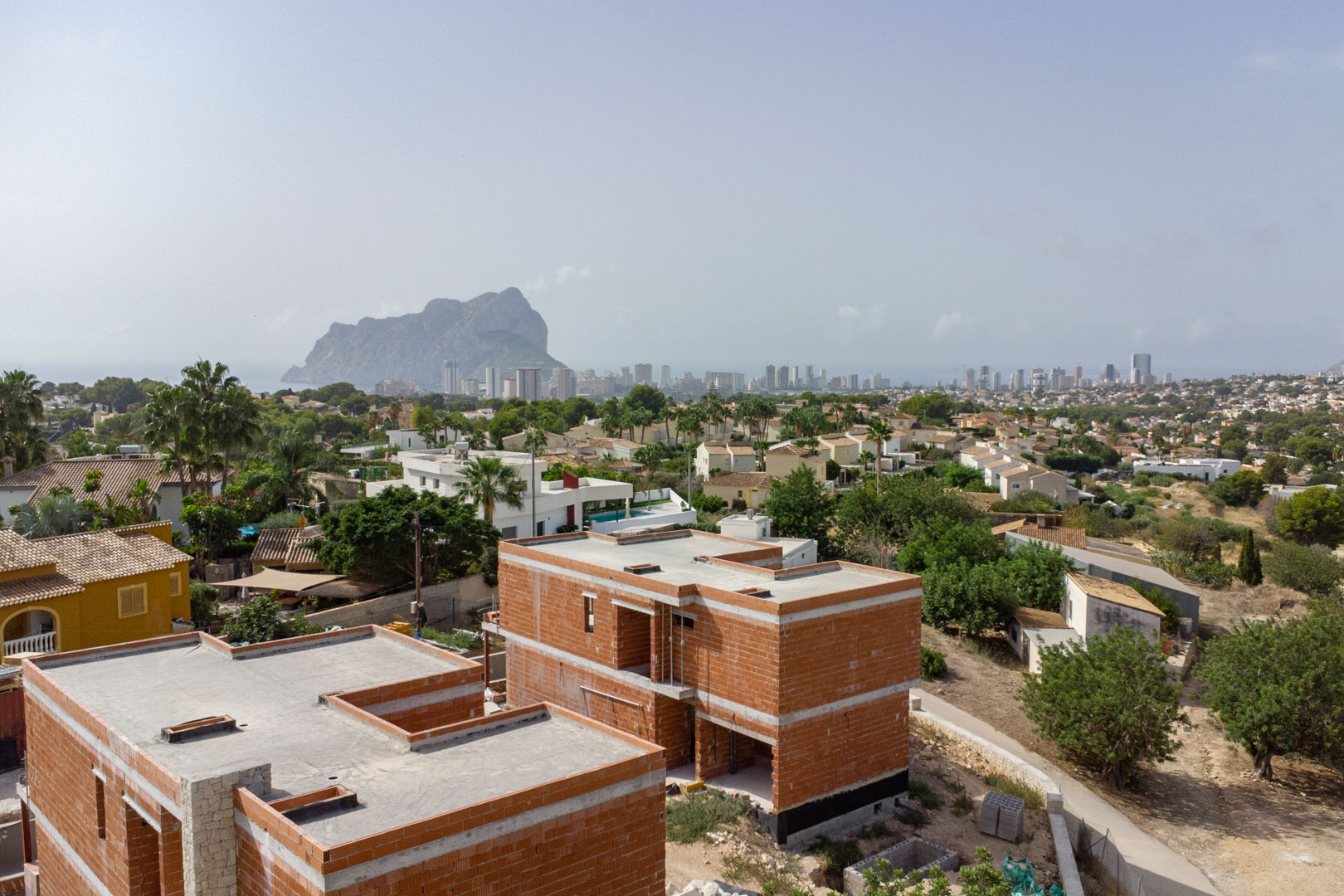 Vue aérienne de la structure en briques des villas en construction, offrant un panorama sur le Peñón de Ifach et la ligne d'horizon de Calpe.