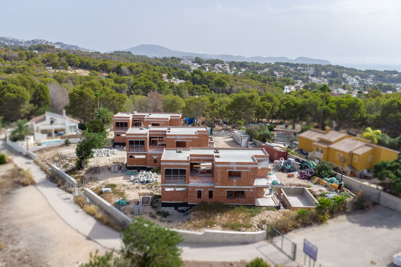 Vue aérienne de l'état d'avancement des trois villas, illustrant les structures en briques, les toits plats et le cadre verdoyant environnant.