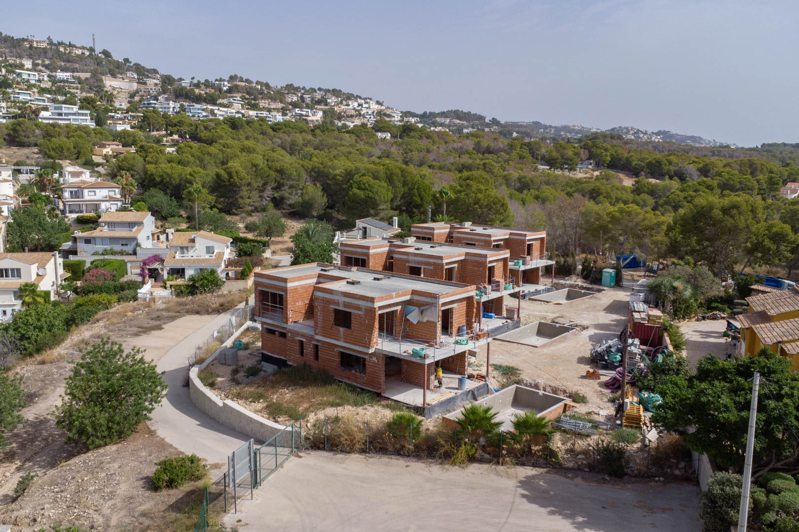 Vue aérienne de l'état d'avancement du chantier des trois villas, mettant en évidence le gros œuvre en briques et les structures des piscines privées en bordure de forêt.