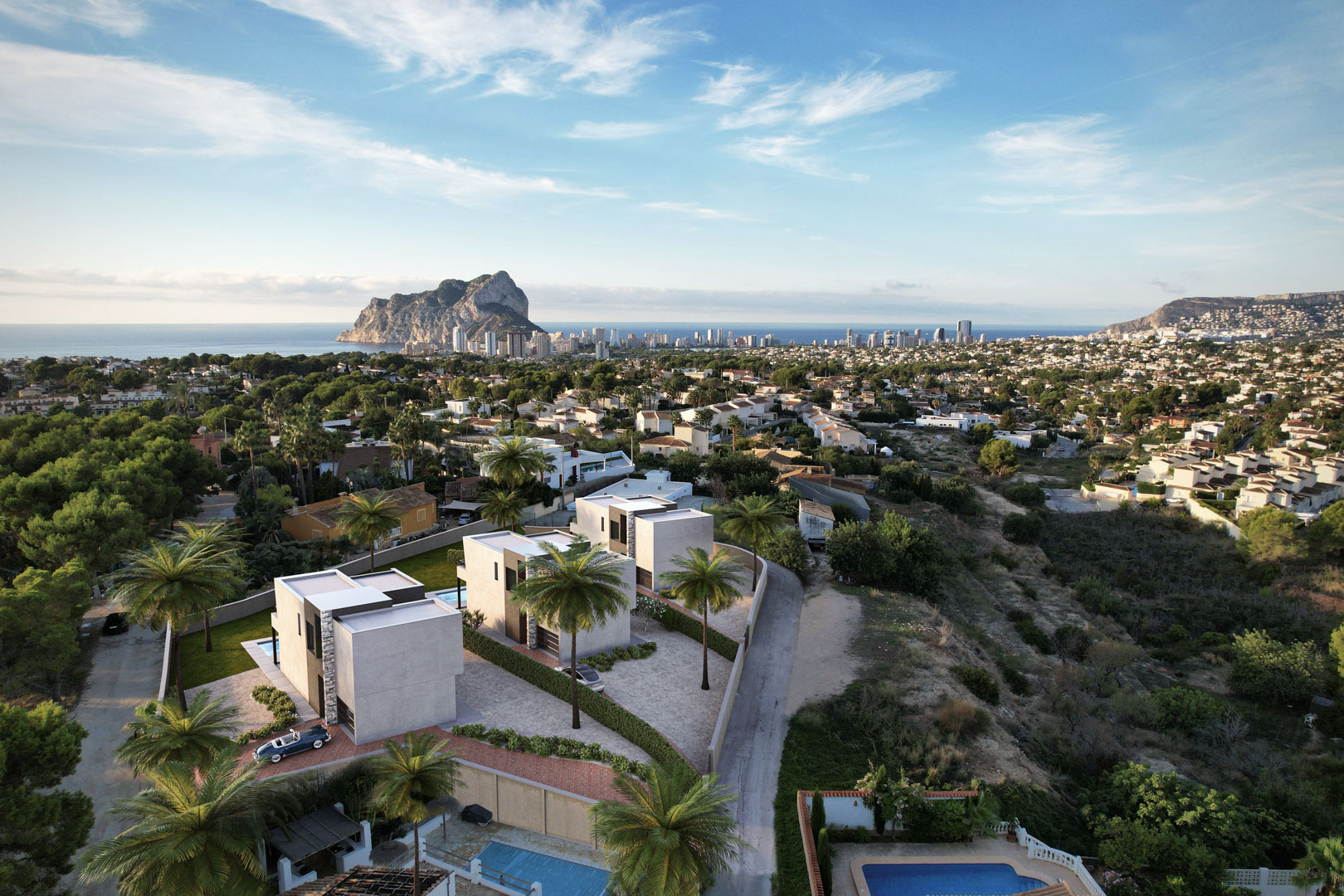 Vue aérienne de trois villas contemporaines à l'architecture cubique, offrant un panorama dégagé sur le Peñón de Ifach et le littoral de Calpe.