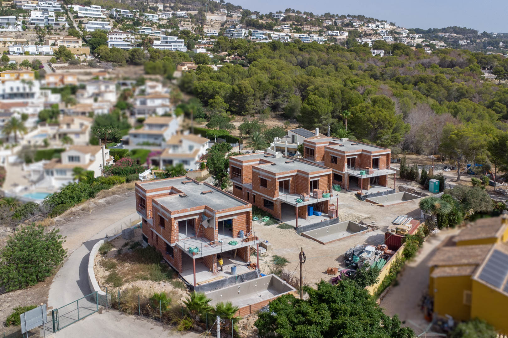 Vue aérienne des trois villas de luxe en phase de gros œuvre, illustrant la structure en briques et les emplacements des piscines privées sur chaque parcelle.