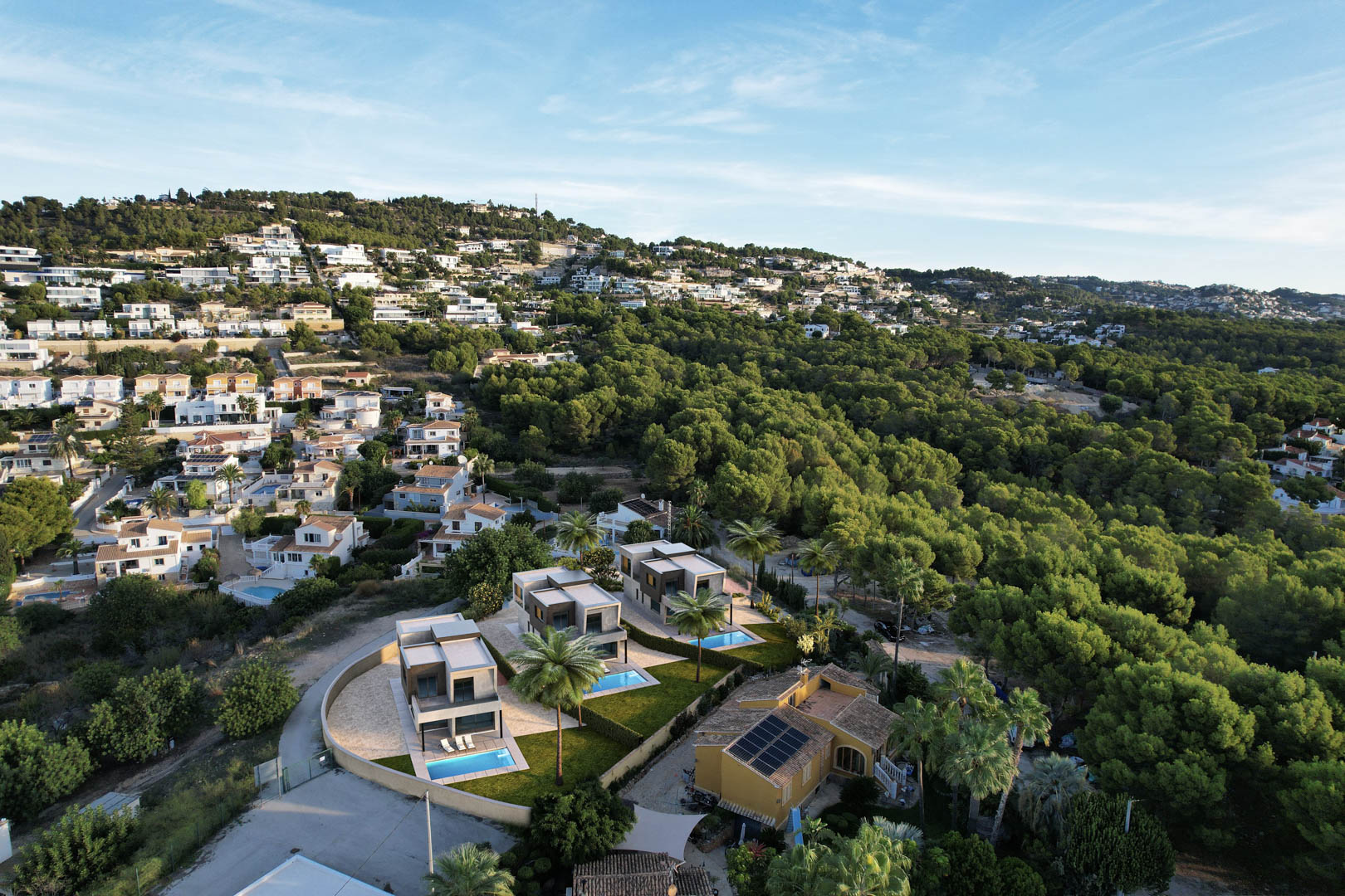 Vue aérienne des trois villas modernes avec piscines privées et jardins, nichées dans un quartier résidentiel bordé par une forêt de pins à Calpe.
