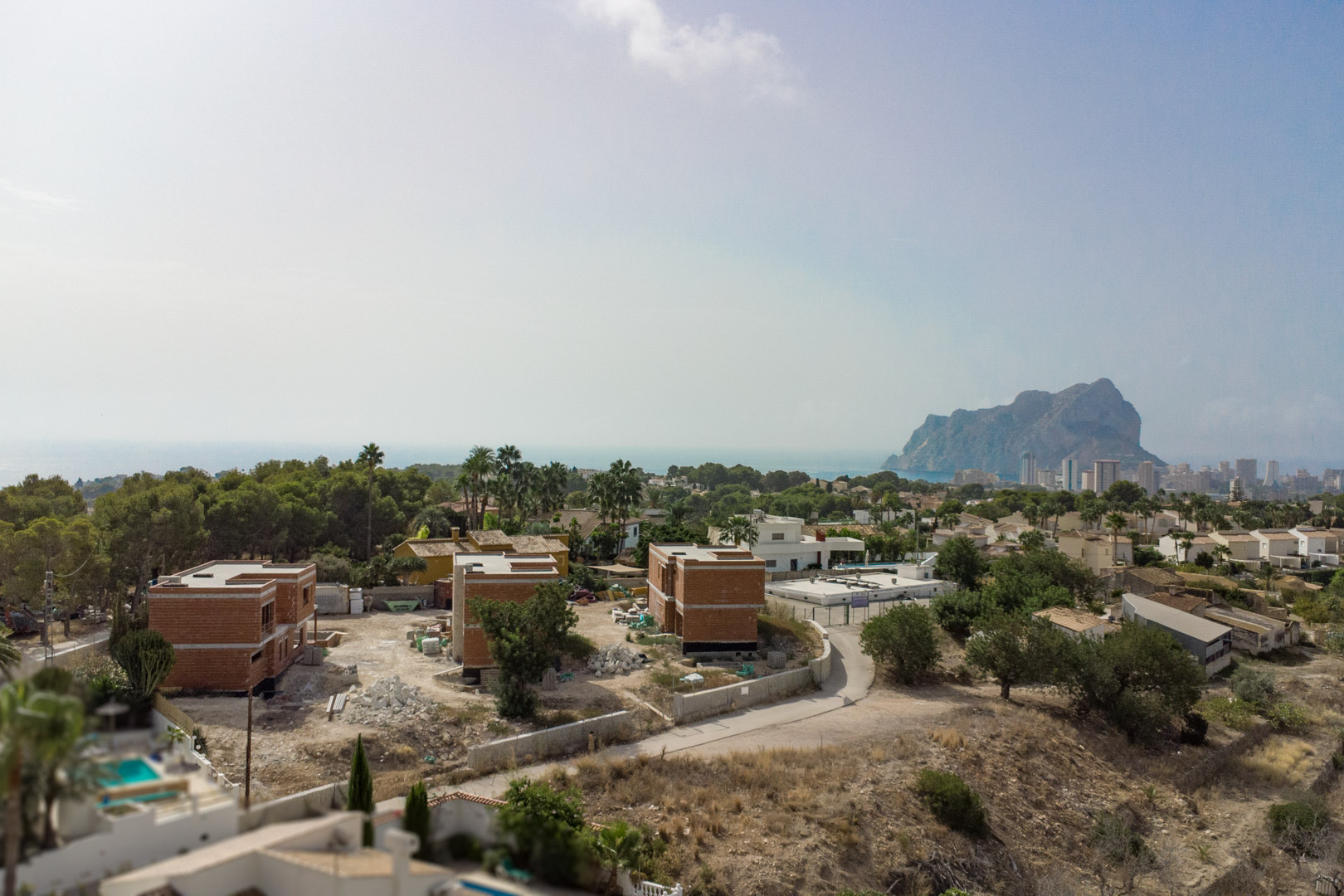 Vue aérienne du chantier des trois villas à Partida Gran Sol, avec le Peñón de Ifach et la silhouette de Calpe en arrière-plan sur la mer Méditerranée.