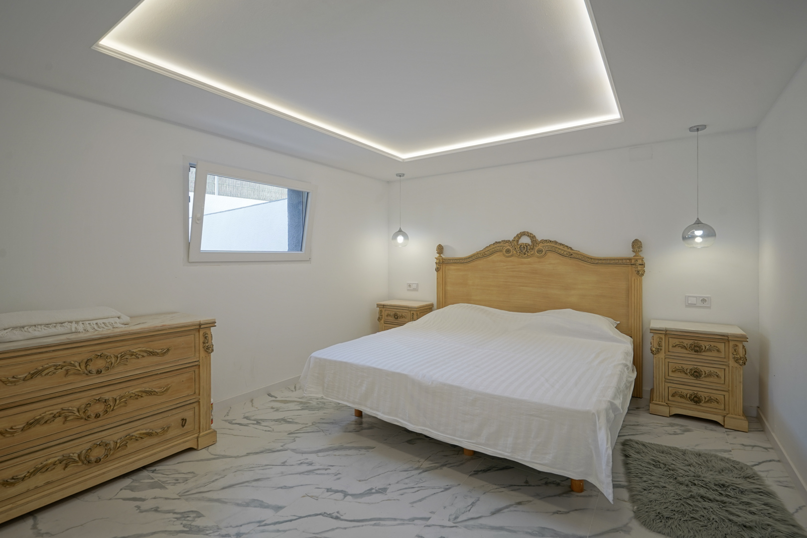 Chambre avec mobilier classique sculpté, sol en grès cérame effet marbre et plafond avec éclairage LED périphérique intégré.