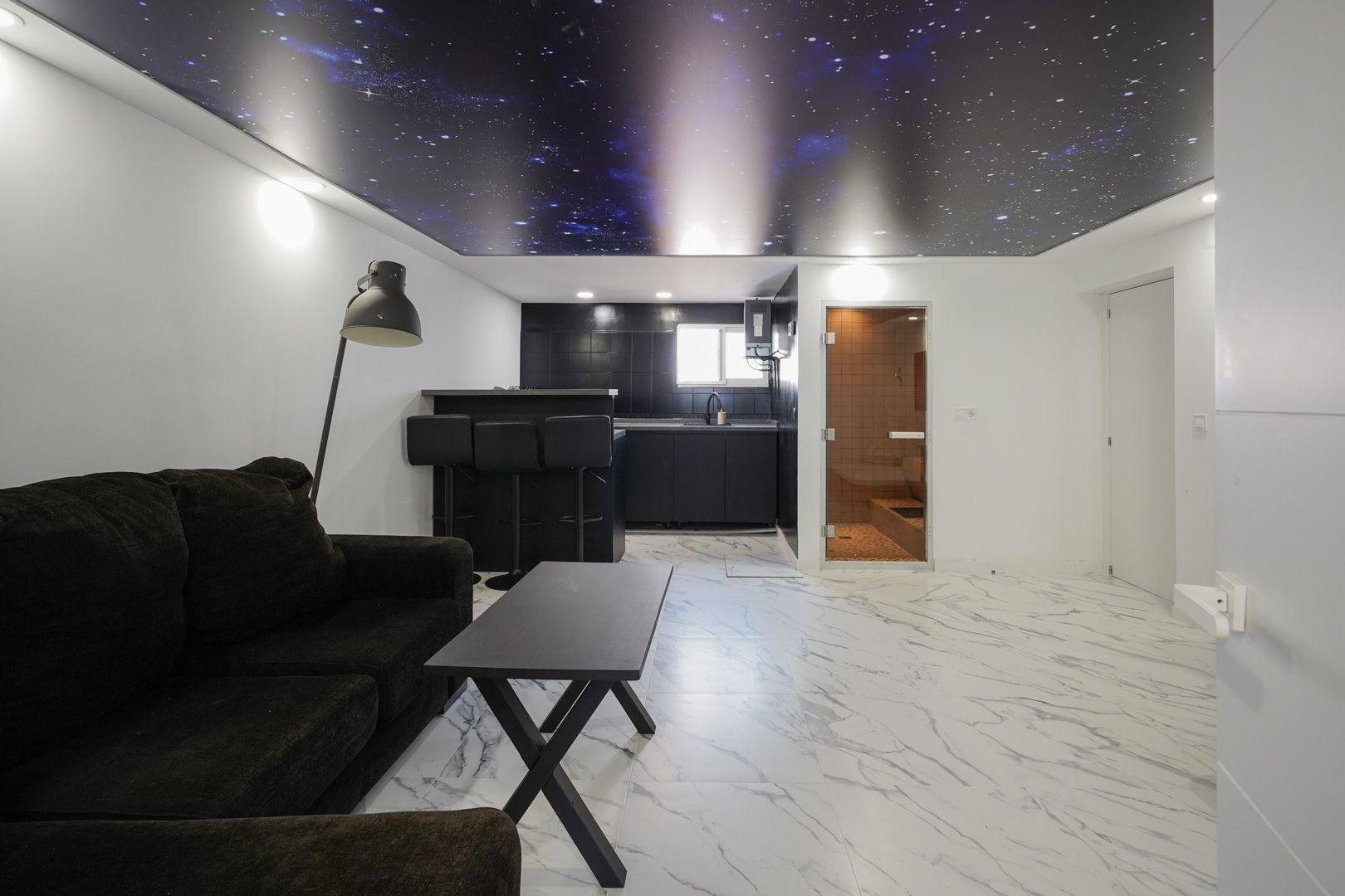 Espace de détente avec kitchenette, sol en grès cérame effet marbre, plafond tendu à motif galaxie et accès à un sauna privé intégré.