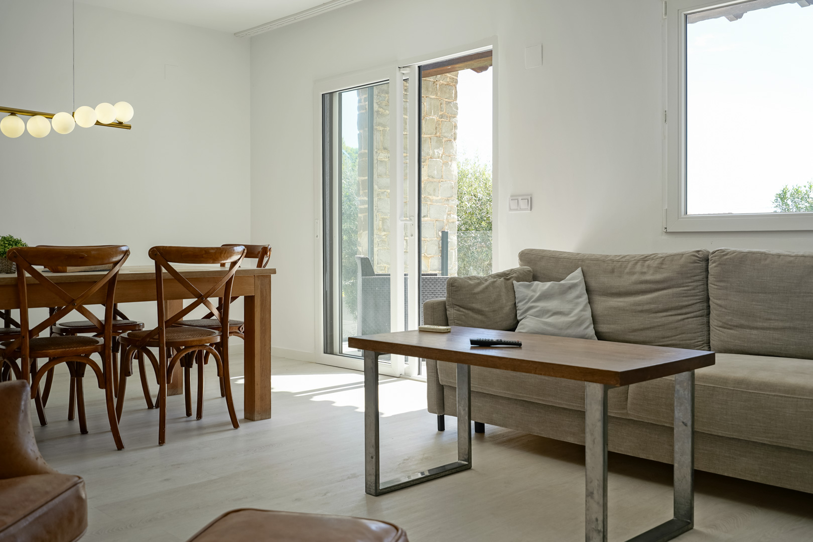 Espace de vie lumineux avec mobilier en bois et luminaire à globes. Les baies vitrées relient l'intérieur à la terrasse en pierre naturelle.