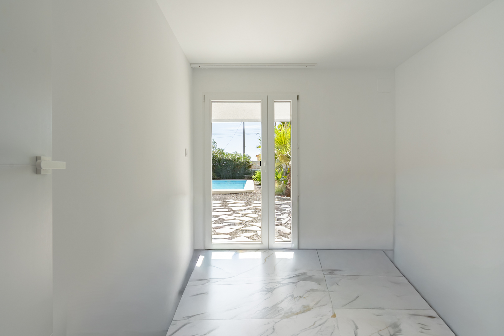 Pièce lumineuse avec sol en grès cérame effet marbre et accès direct à la terrasse de la piscine par une porte vitrée.