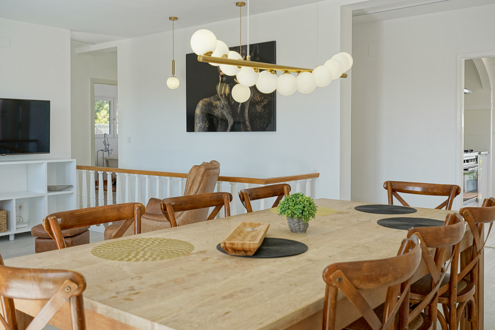 Salle à manger lumineuse avec table en bois massif et chaises croisées, agrémentée d'un luminaire design et d'un accès ouvert vers le salon et l'escalier.