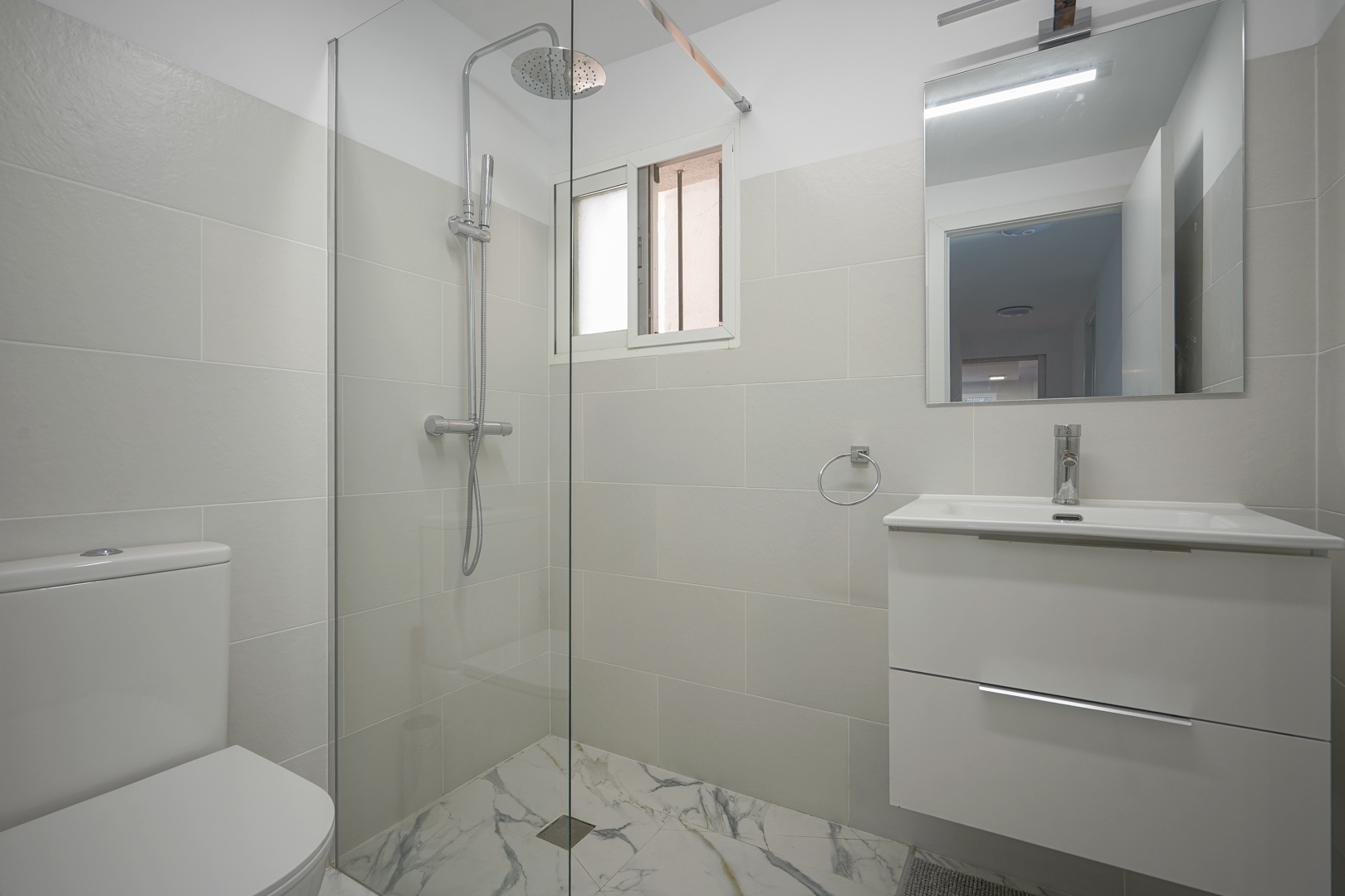Salle de bains moderne avec douche à l'italienne, paroi en verre, meuble vasque blanc et carrelage au sol effet marbre.