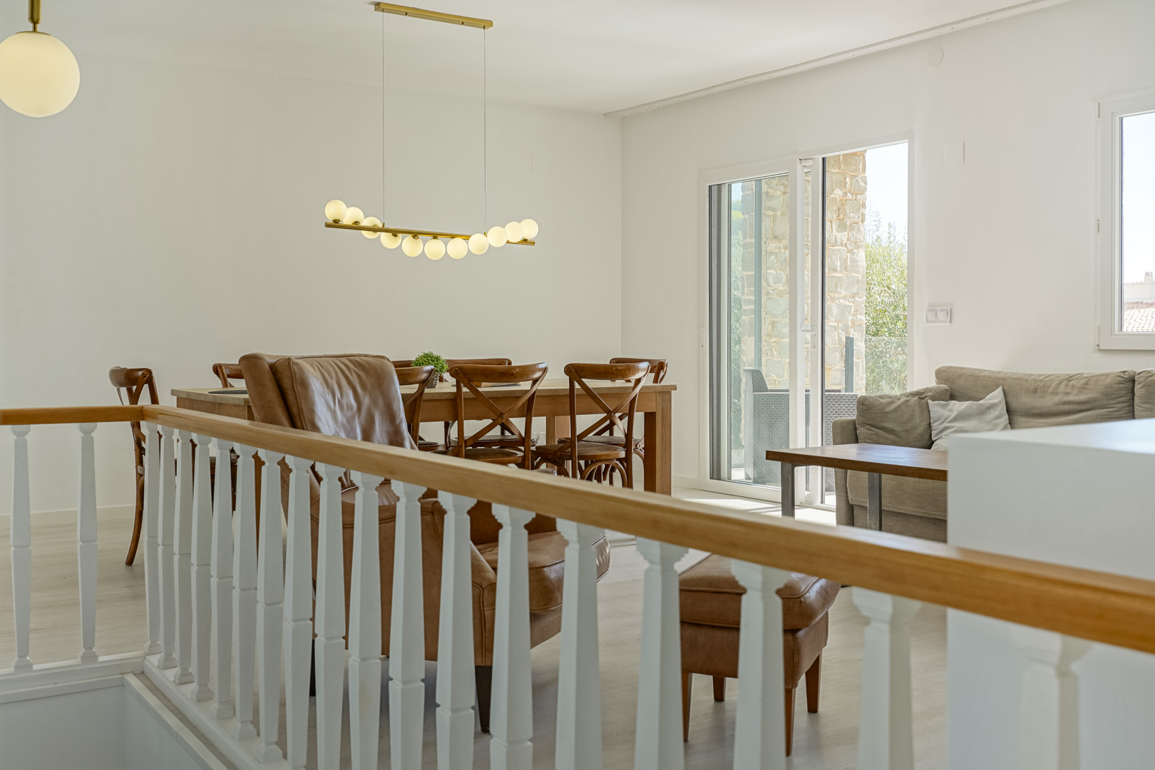 Salon-salle à manger lumineux avec balustrade blanche, mobilier en bois, luminaire design et accès direct à la terrasse par une baie vitrée.