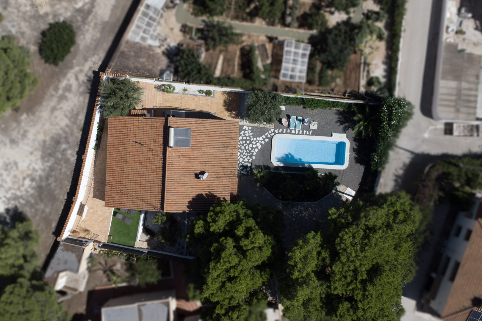 Vue aérienne de la propriété révélant l'agencement du terrain, la piscine rectangulaire, les terrasses en terre cuite et le panneau solaire sur le toit.