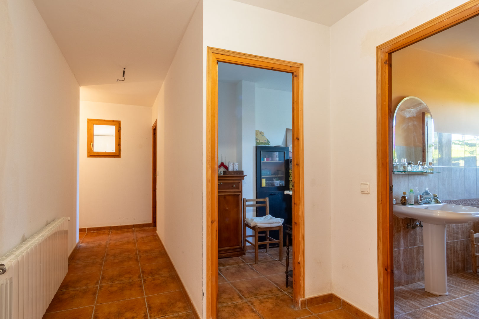 Couloir de distribution avec sol en grès rustique et encadrements en bois, desservant une salle de bain et plusieurs pièces équipées de radiateurs.
